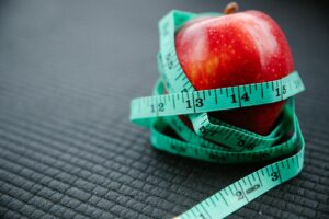 A vibrant red apple encircled by a blue measuring tape, symbolizing health and weight management.