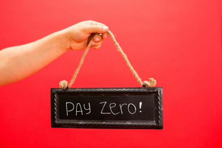 A hand holds a sign displaying 'Pay Zero' on a vibrant red background, emphasizing a free or zero-cost concept.